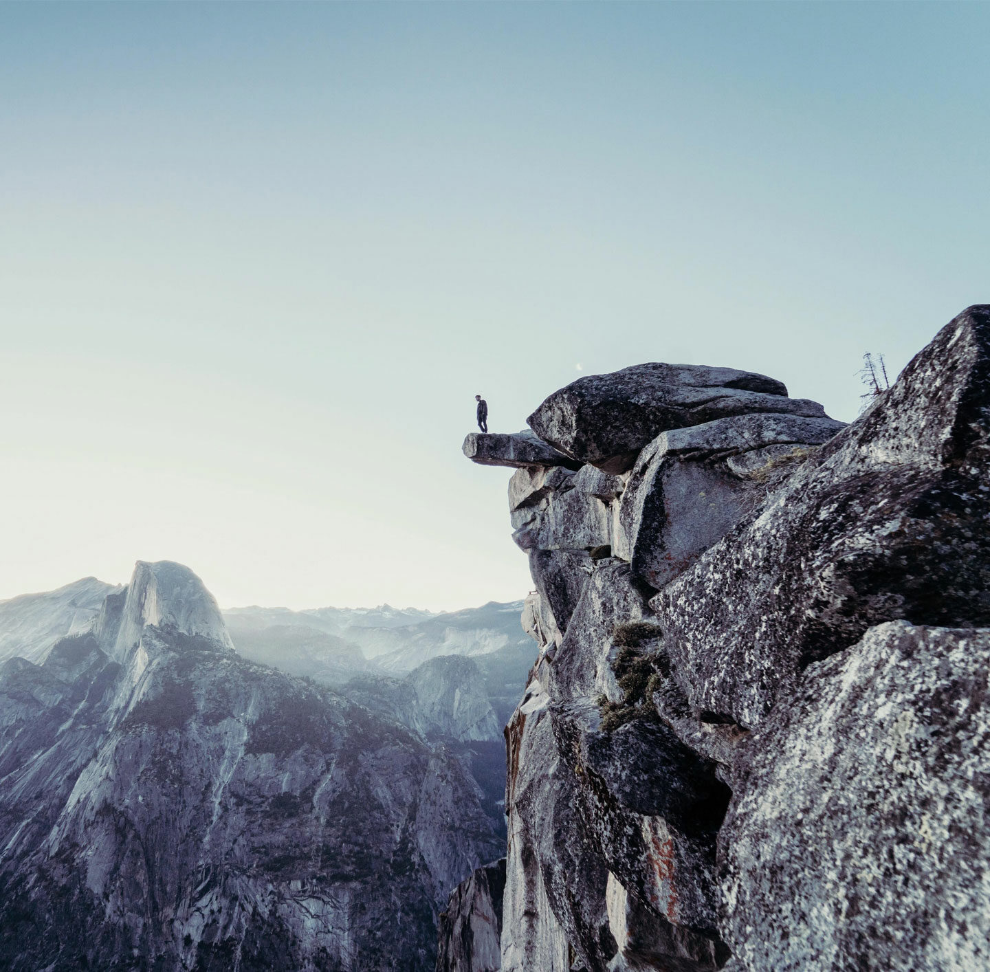Umgeben von Gebirge steht eine Person auf einem Felsvorsprung.