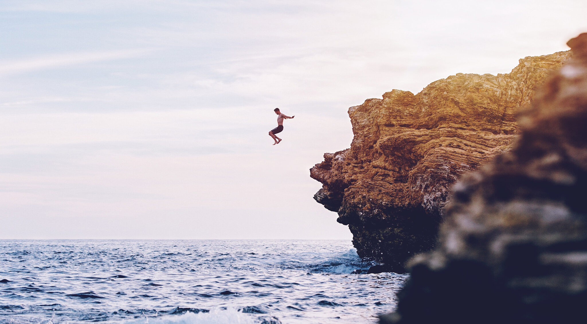 Mann springt von einer Klippe ins Meer.