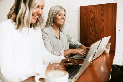 Zwei lachende Frauen beim Arbeiten am Laptop.