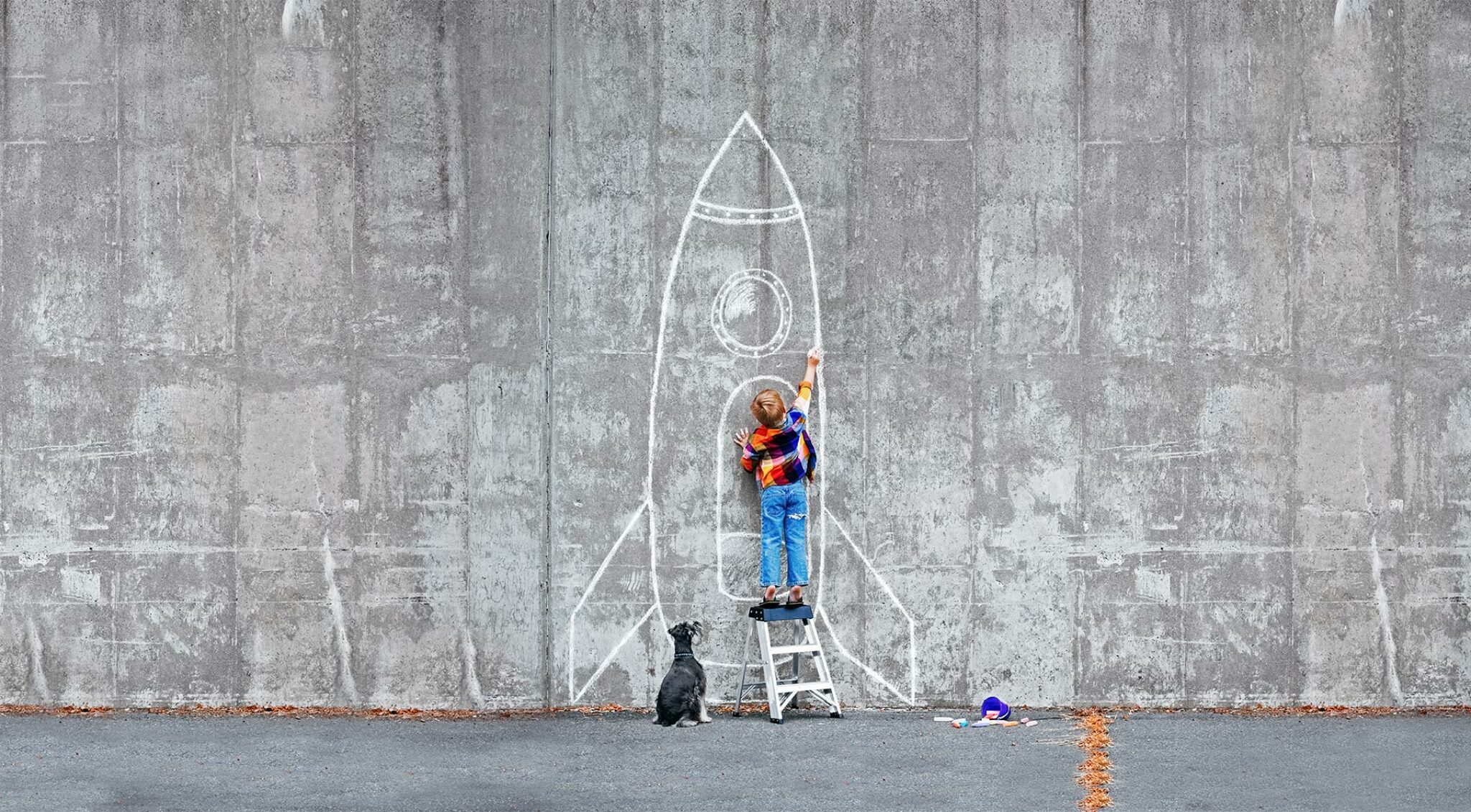 Mit Kreise malt ein Junge eine große Rakete an eine graue Wand.
