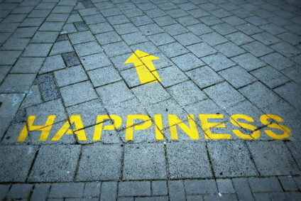 Auf Kopfsteinpflaster steht in gelber Schrift "Happiness", darüber ein Pfeil.
