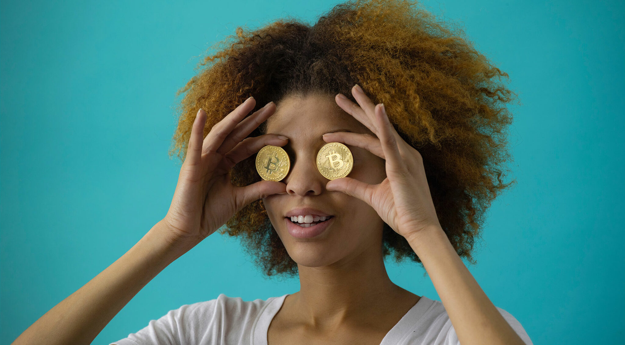 Eine Frau hält sich zwei Münzen mit Bitcoin-Logo vor die Augen.