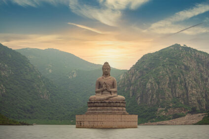 Große Buddha-Statue vor einen grünen, hügeligen Landschaft.
