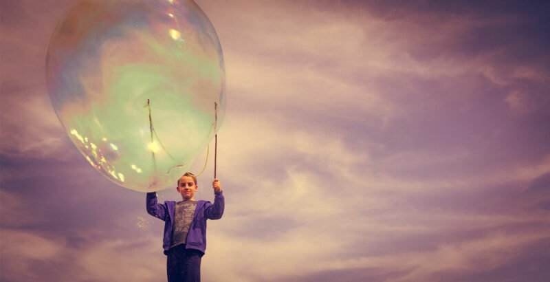 Kind hält Riesenseifenblase an zwei Stöcken.