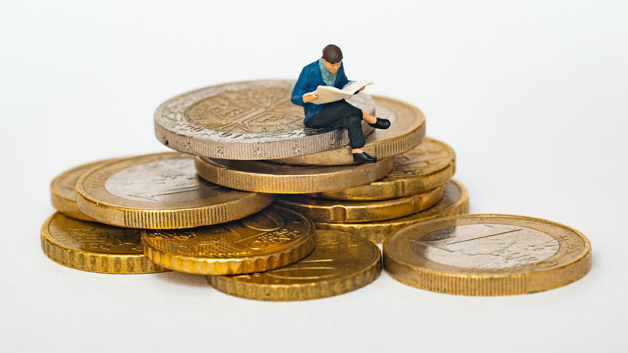 Modellfigur sitzt auf einem Haufen Euro-Münzen