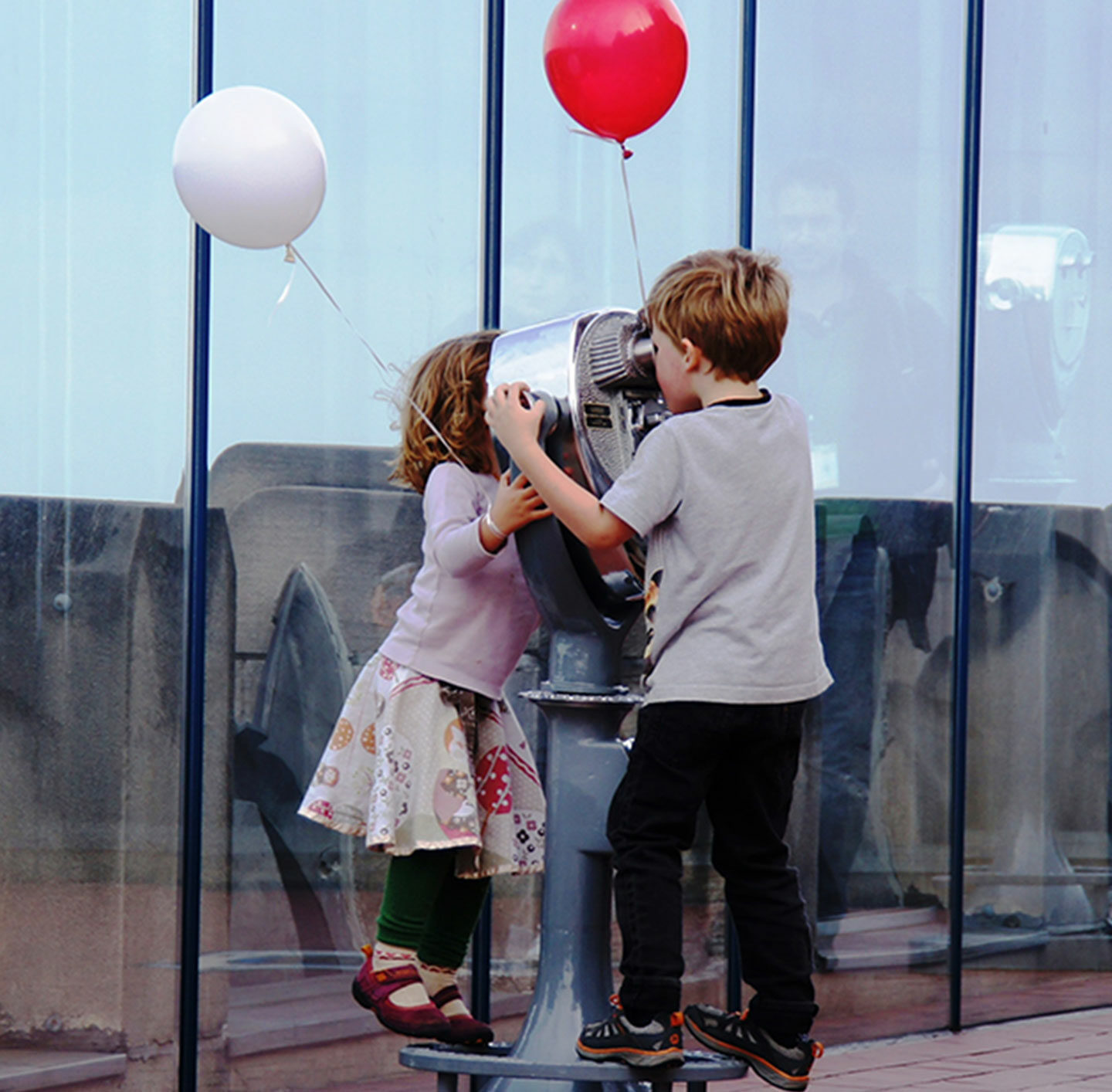 Zwei kleine Kinder mit Luftballons am Fernglas.