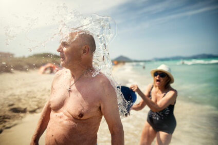 Frau übergießt Mann mit Wasser am Strand