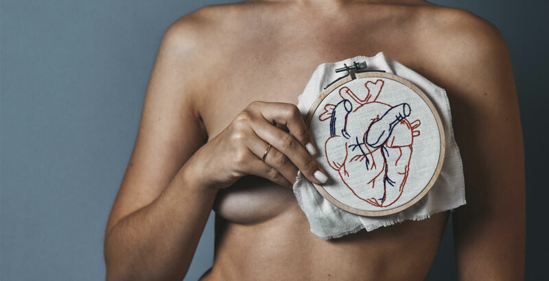 Frau hält Stickerei mit Herz vor Ihre Brust