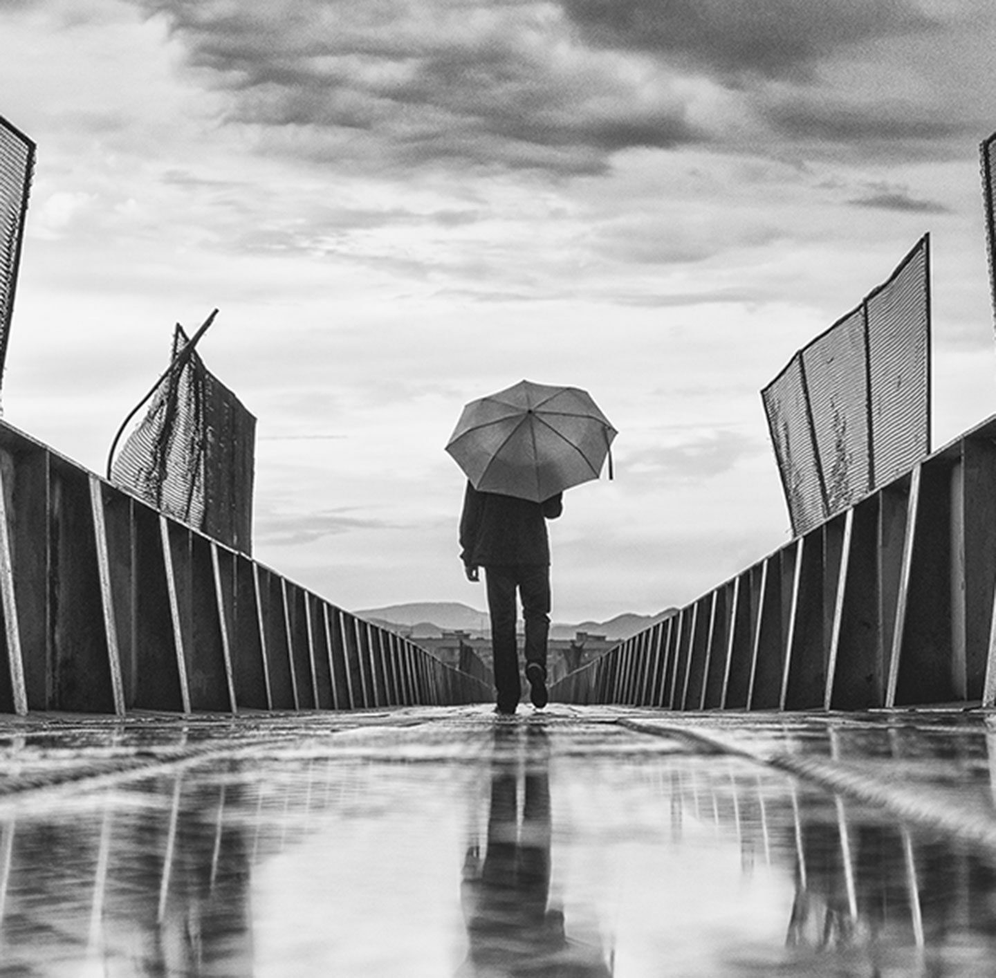 Ein Mensch geht mit einem Regenschirm über die Brücke