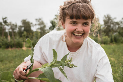 Junge Frau lacht mit Pflanze in der Hand.