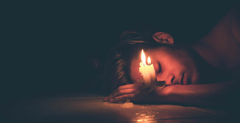 Ein Mann schläft - zwei Kerzen brennen auf seiner Hand