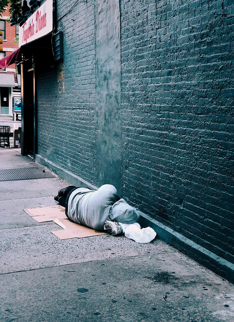 Ein Mensch schläft an einer Mauer mit Zeitungen als Kopfkissen