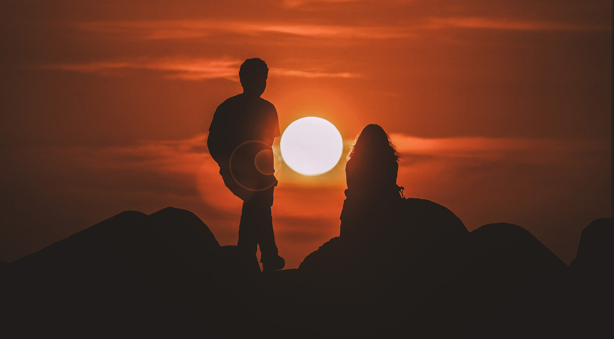 Zwei Menschen am Berggipfel vor Sonnenuntergang.