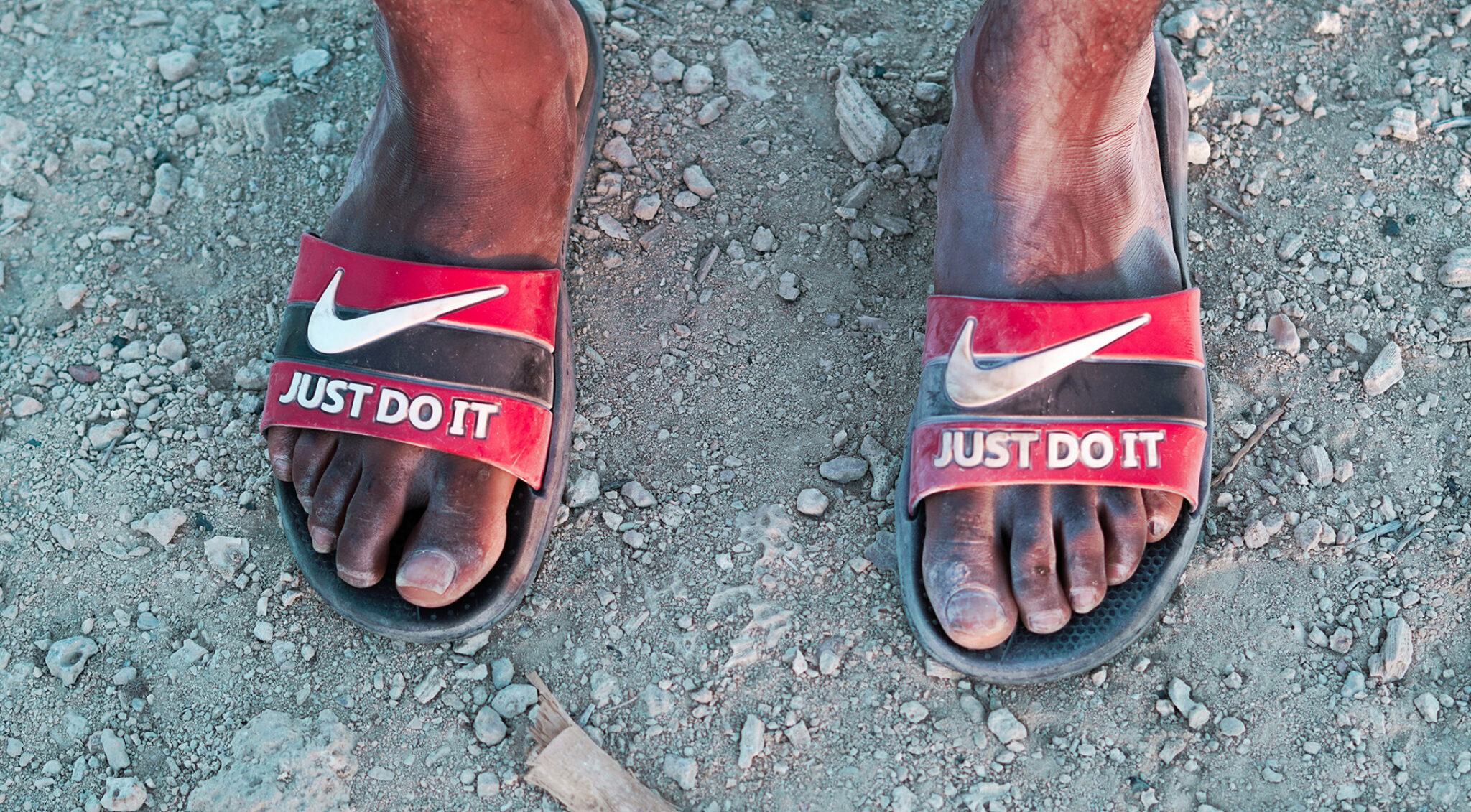 Nackte Füße einer Person of Colour mit Nike-Badeschuhen auf denen Just do it steht
