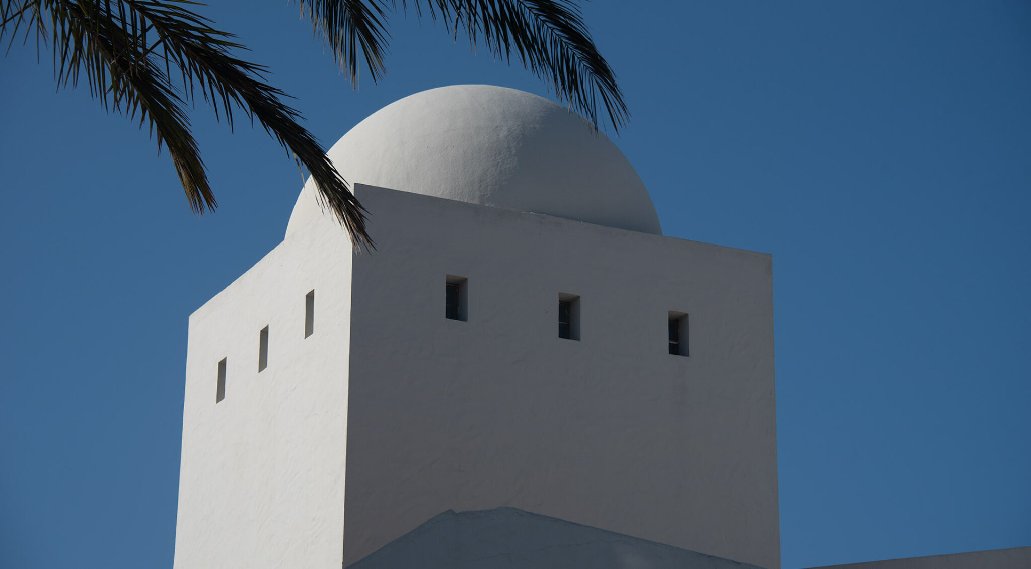 Minarettkuppel mit kleinen Fenstern vor blauem Himmel