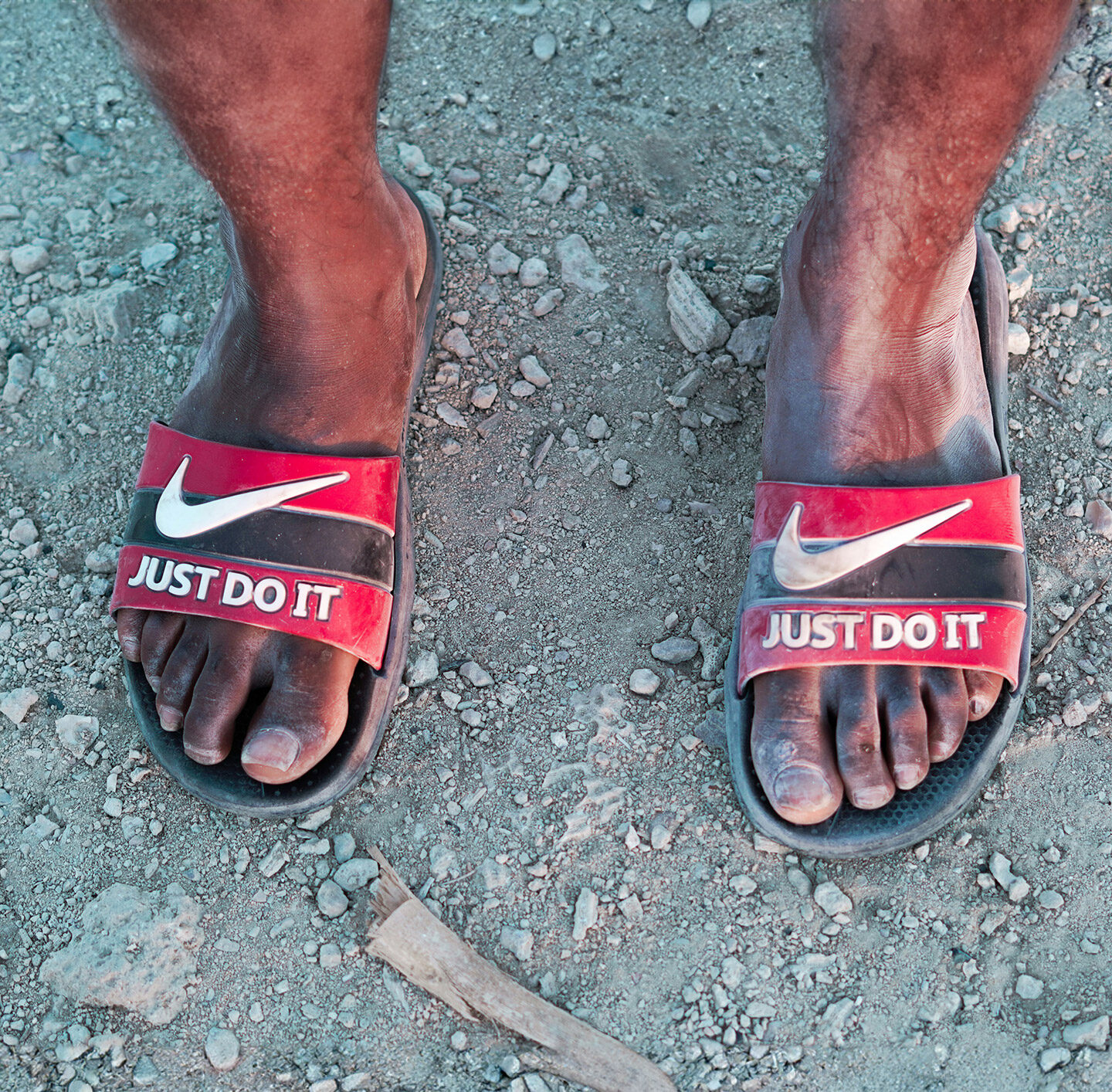 Nackte Füße einer Person of Colour mit Nike-Badeschuhen auf denen Just do it steht