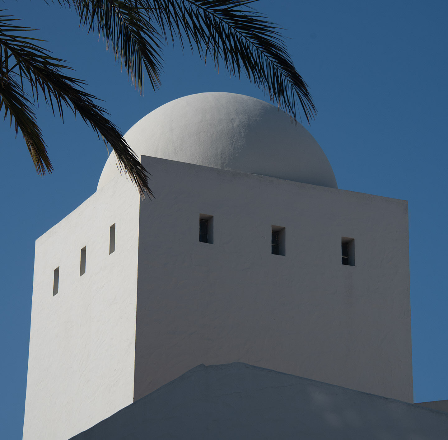 Minarettkuppel mit kleinen Fenstern vor blauem Himmel