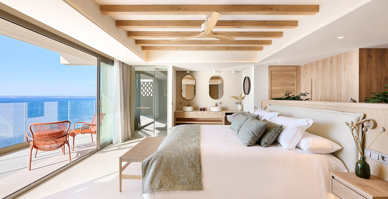 Blick in ein Zimmer des Hotels „Iberostar Selection Es Trenc, in hellen Farben und Materialien eingerichtet und mit Holzbalken an der Decke