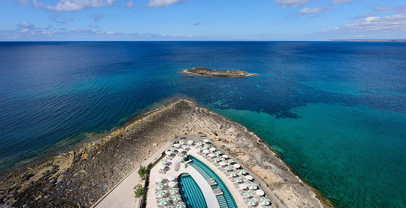 Blick aus der Vogelperspektive auf die Poollandschaft des Hotels „Iberostar Selection Es Trenc und das offene Meer