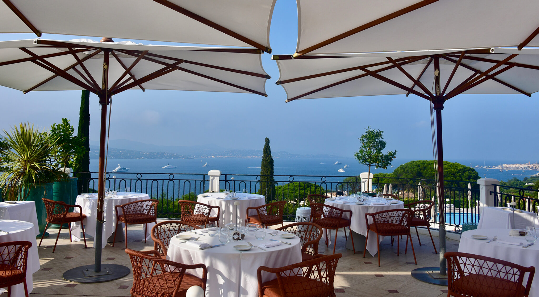 Blick von der Terrasse des Hotels Althoff Villa Belrose mit weißen Sonnenschirmen und gedeckten Tischen auf die Bucht von Saint-Tropez.