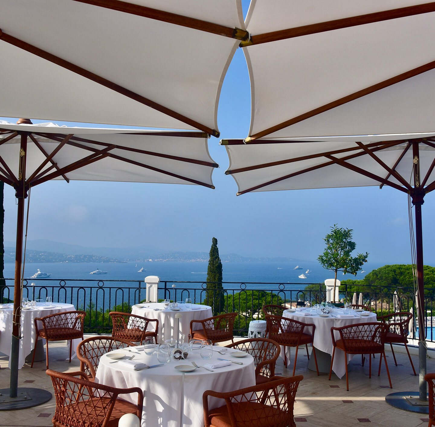 Blick von der Terrasse des Hotels Althoff Villa Belrose mit weißen Sonnenschirmen und gedeckten Tischen auf die Bucht von Saint-Tropez.