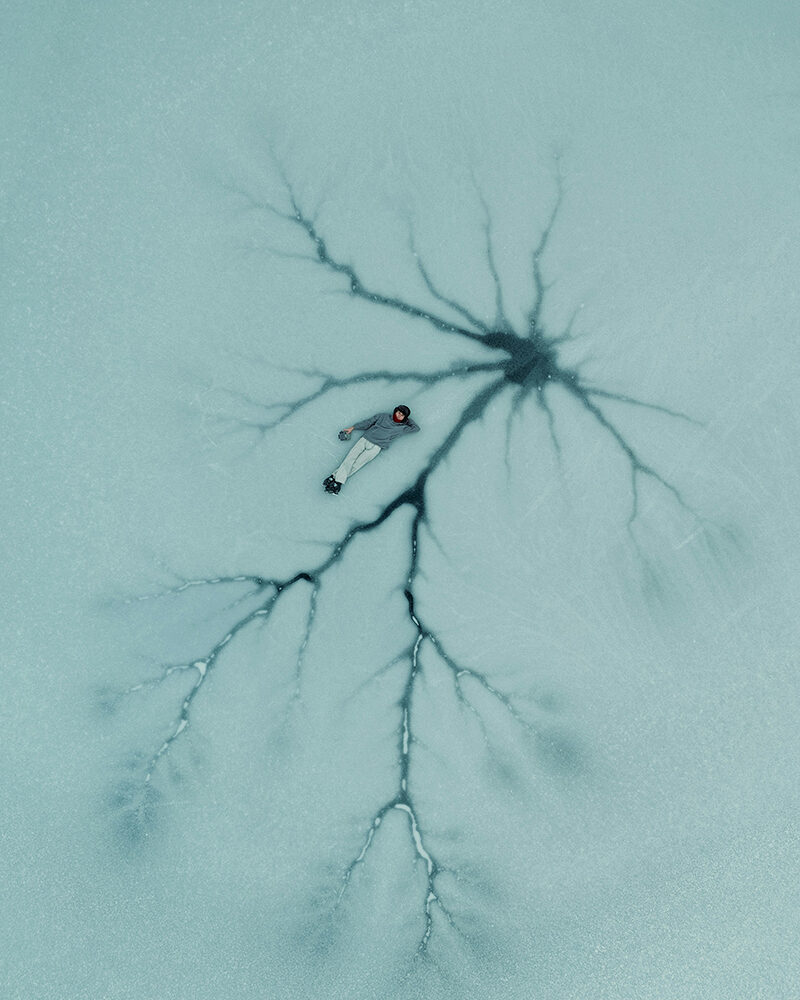 Aus der Vogelperspektive: Eine Person liegt auf einer bläuchlich gefärbten Eisfläche