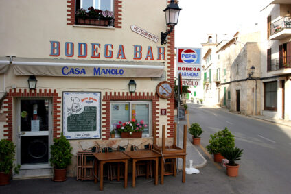 Blick von außen auf die Bodega Barahona in Mallorca. Ein beigefarbenes Haus mit dunkelroten, gezackten Bemalungen der Fenster und Türen.