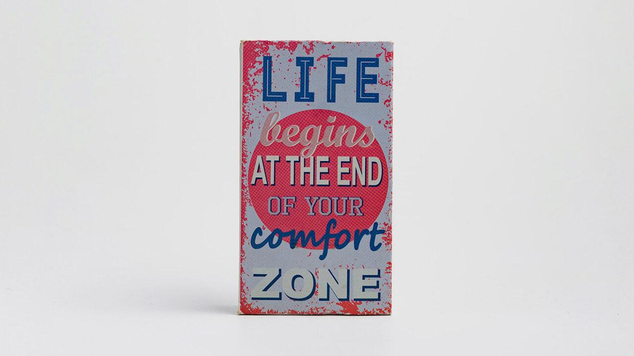 Ein altes blau-rot-weisses Blechschild mit der Aufschrift "Life begins at the End of your comfort Zone"