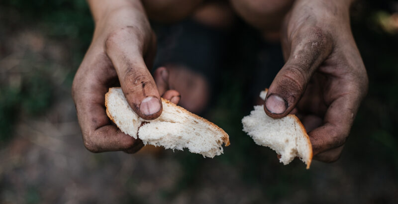 Zwei schmutzige Hände teilen ein Stück Brot