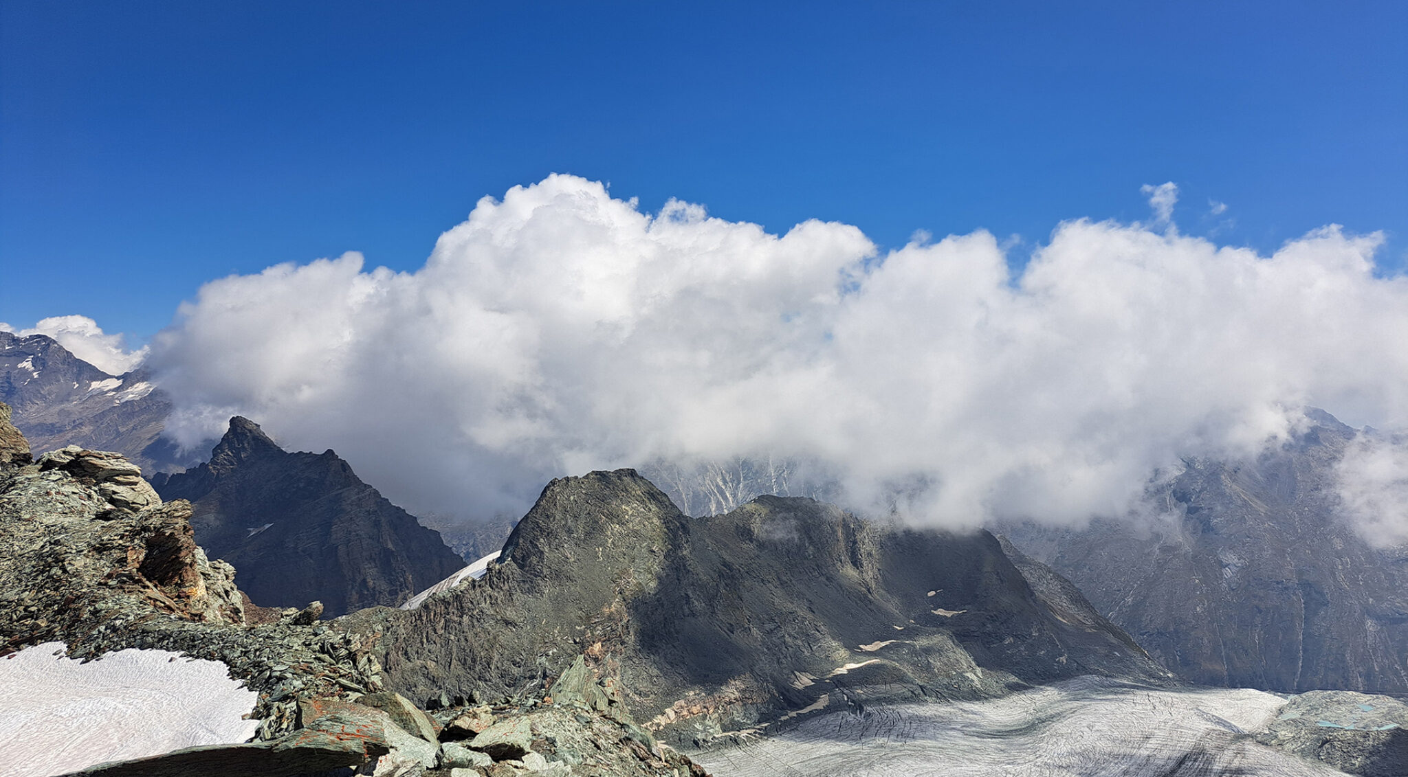 Panoramaaufnahme von Bergen mit Wolken über den Gipfeln.