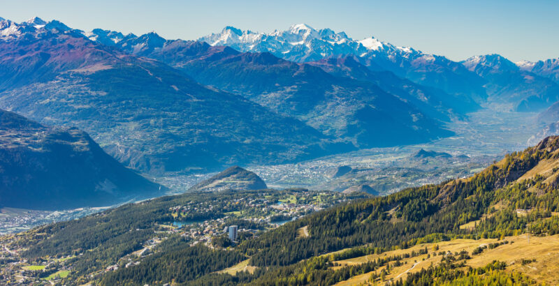 Weitläufige Landschaft im Wallis mit Feldern, Bäumen und Bergen im Hintergrund.