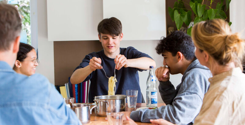 Fünf Personen sitzen am Tisch und essen zusammen.