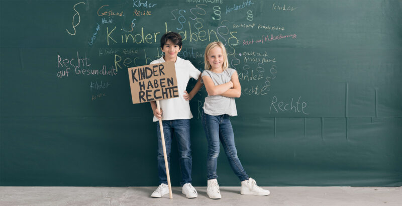 Zwei Kinder stehen vor grüner Schultafel und halten ein Pappschild mit Stil in der Hand.