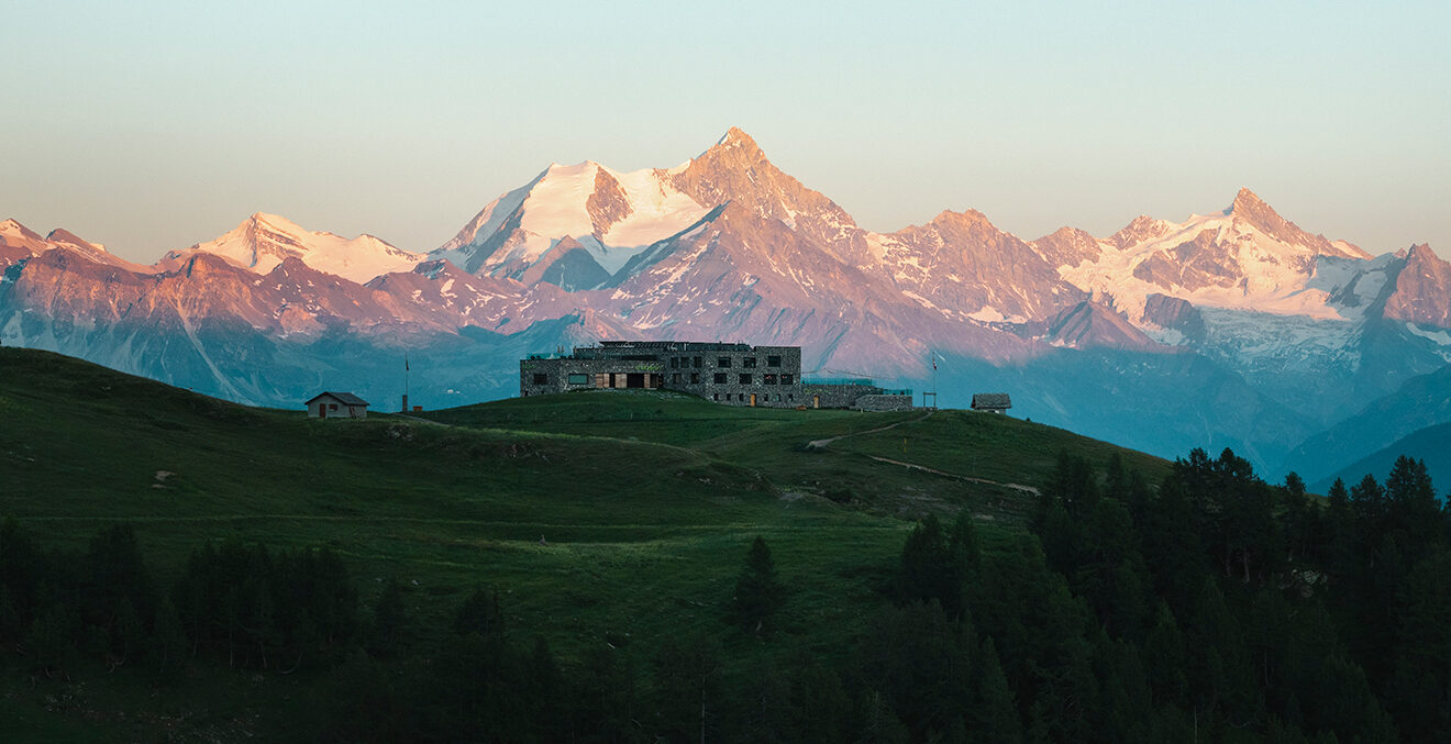 Blick aus der ferne auf das GUARDA GOLF vor von der Sonne angestrahlter Bergkulisse.
