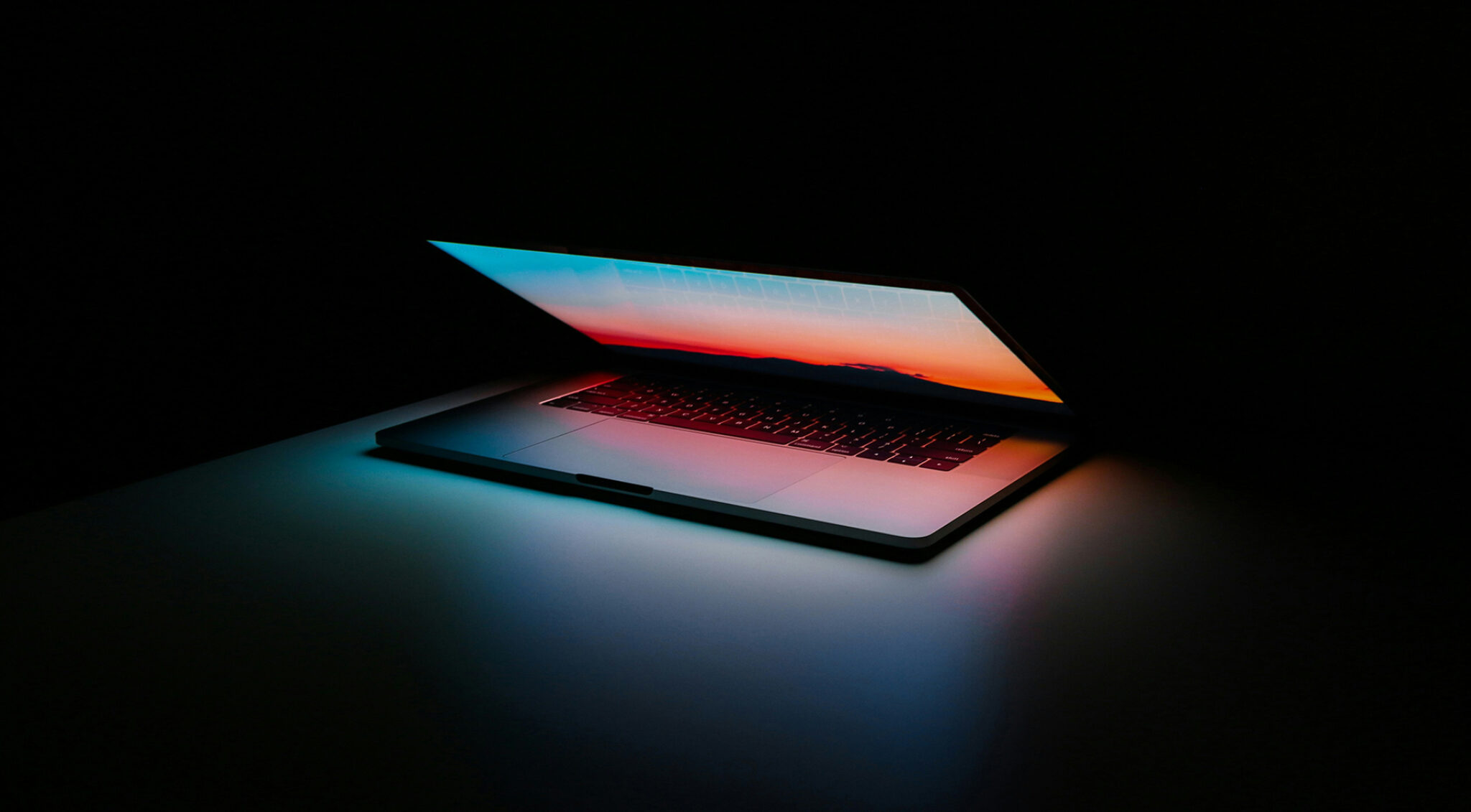 Bildschirm eines halb aufgeklappten Laptops leuchtet in blau und orange in einen schwarzen Raum.