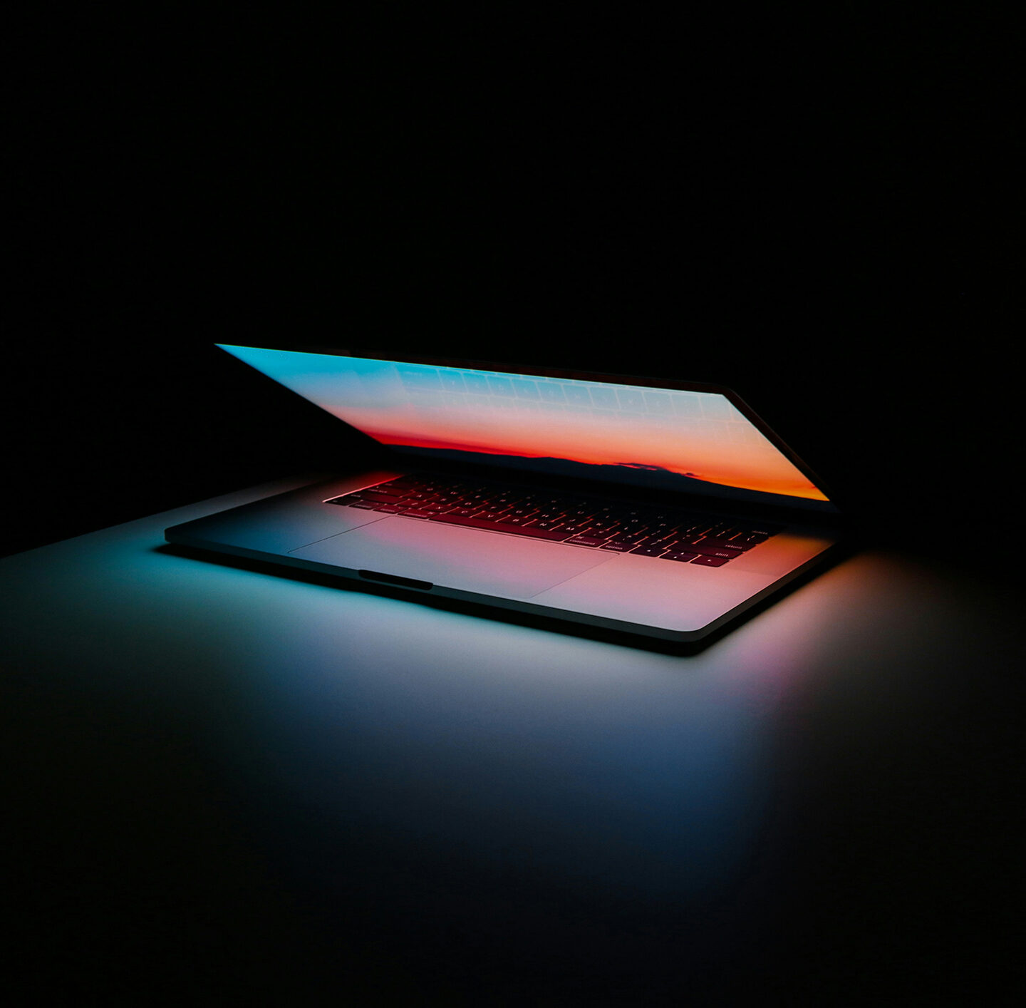 Bildschirm eines halb aufgeklappten Laptops leuchtet in blau und orange in einen schwarzen Raum.