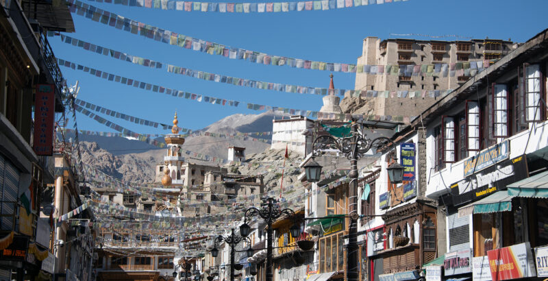 Häuser durch bunte Gebetsfahnen verbunden vor strahlend blauem Himmel in Leh, der Hauptstadt von Ladakh.