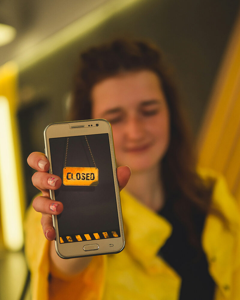 Frau hält ihr Smartphone mit der Aufschrift ‚Closed‘ hoch, um digitale Achtsamkeit und bewusste Offline-Zeiten zu signalisieren.