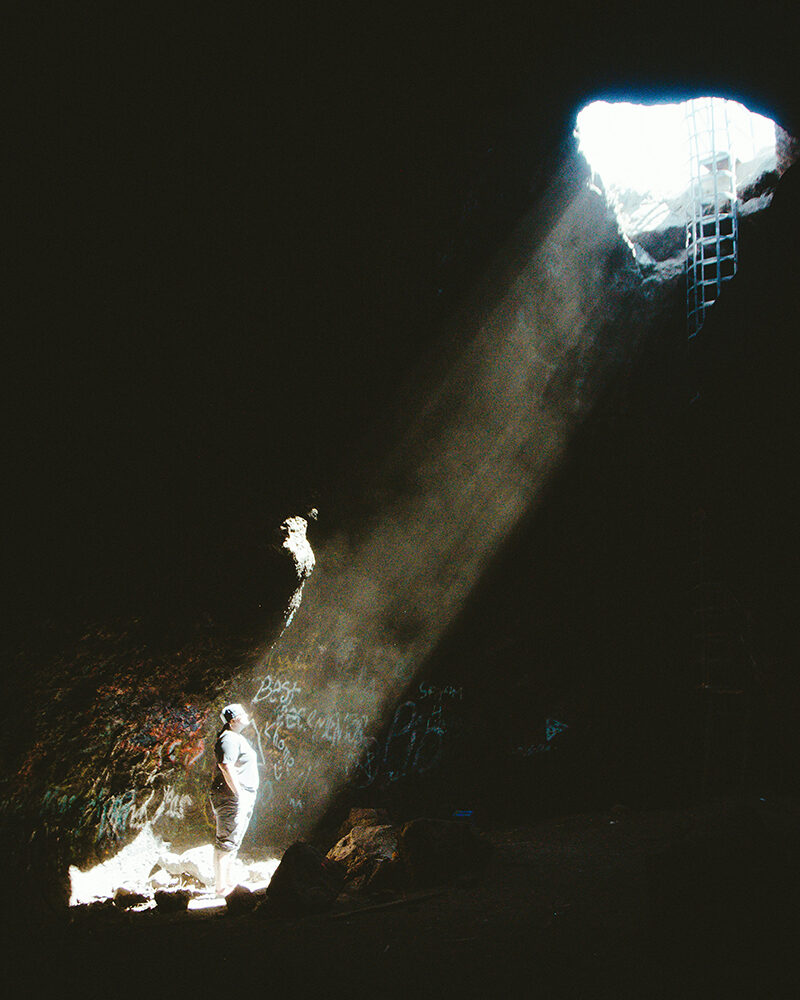 Person in heller Kleidung steht in einer dunklen Höhle unter einem Lichtkegel, der von oben einfällt.