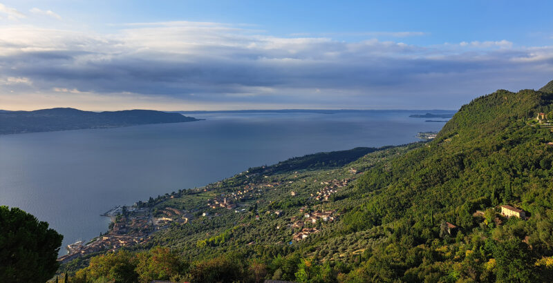 Blick auf die hügelige Landschaft am Gardasee mit Olivenbäumen und blauem Wasser im Hintergrund.