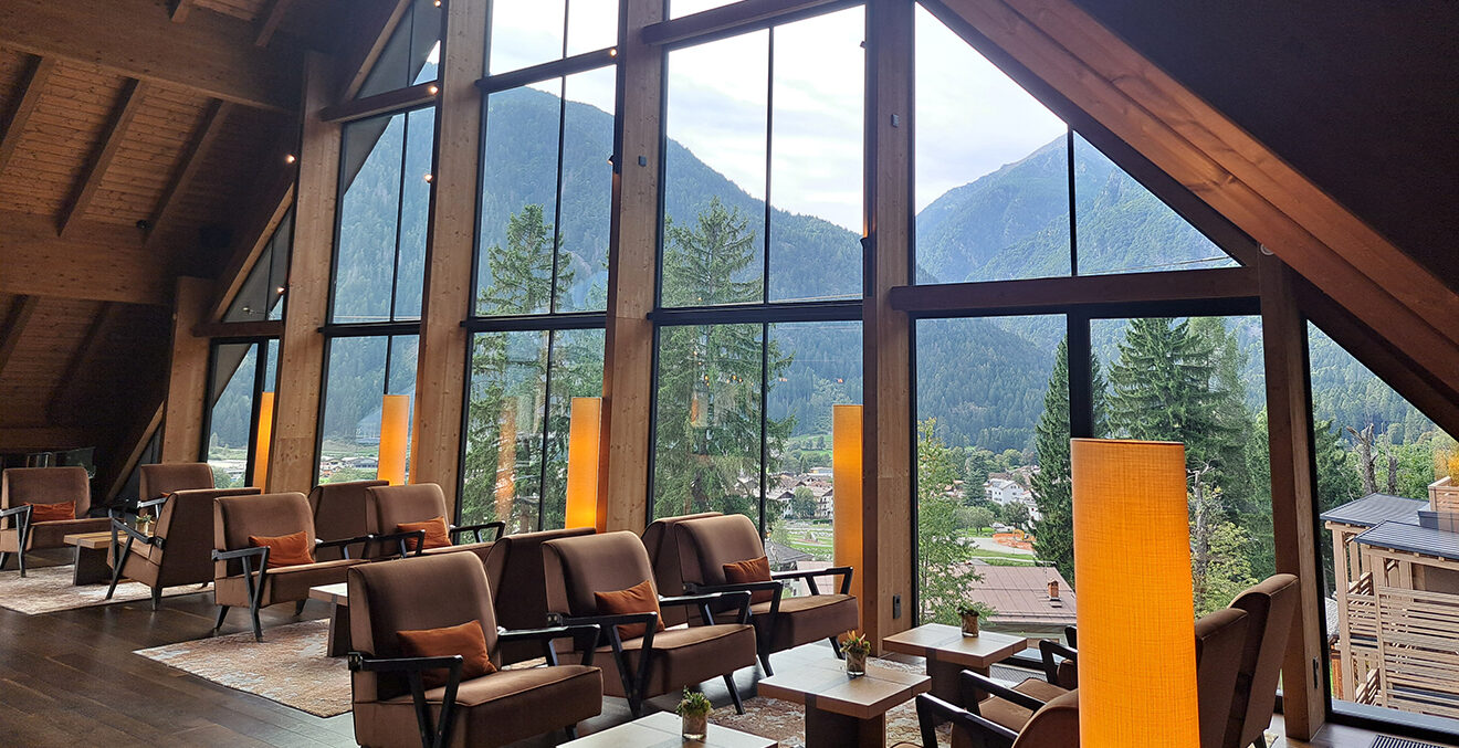 Lounge des Lefay Resorts mit braunen Sesseln und kleinen Tischen vor großer Fensterfront.
