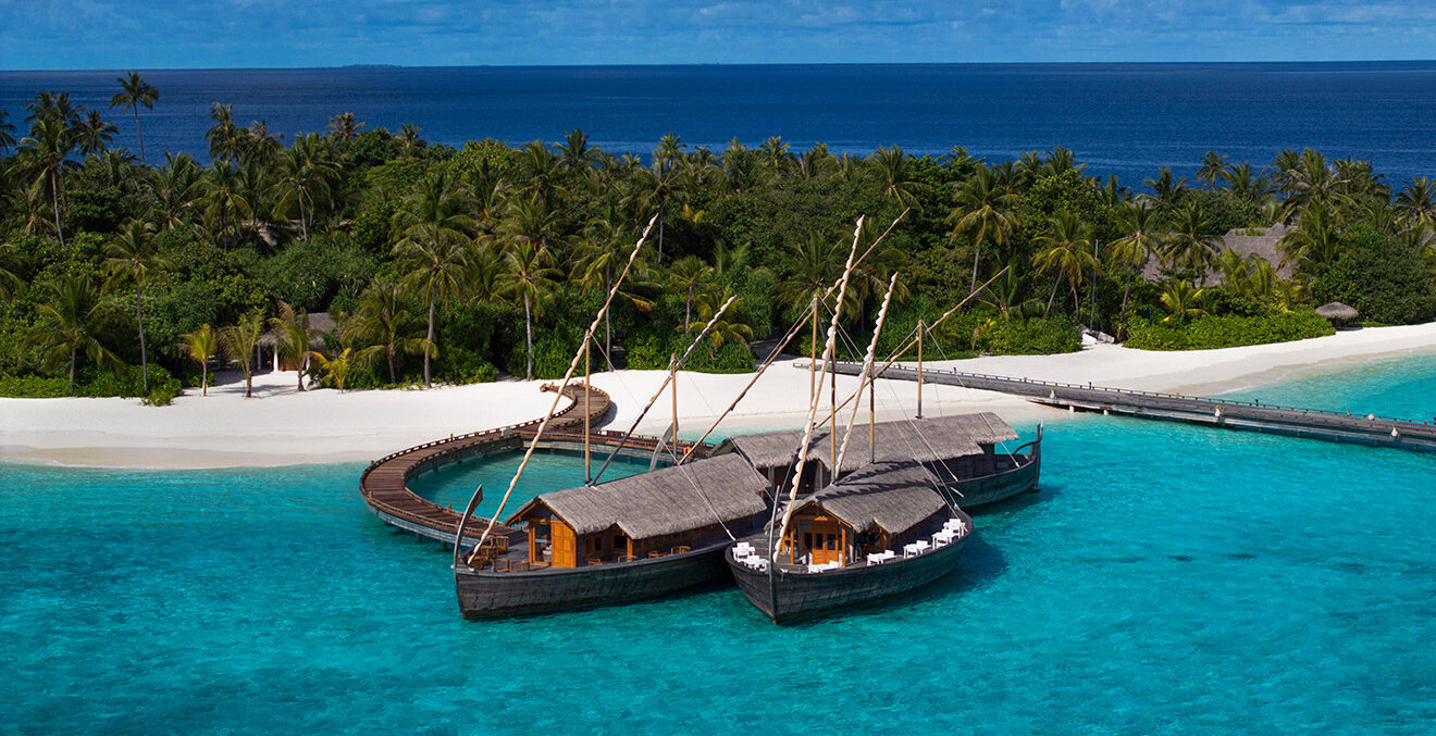 Weißer Strand mit Holzbooten und Bäumen im Hintergrund.