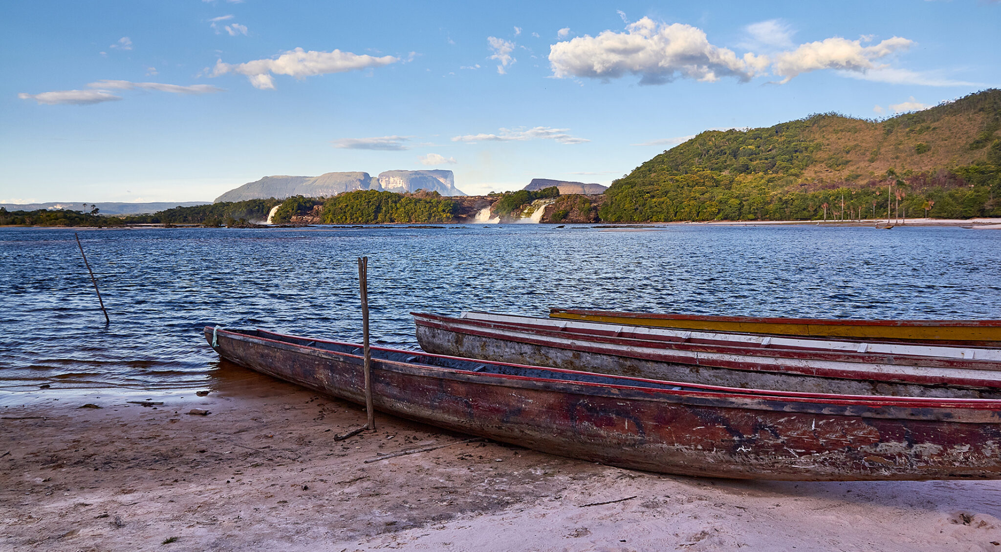 Holzboot am Ufer eines breiten Flusses, umgeben von weiter Landschaft mit bewachsenen Uferzonen.