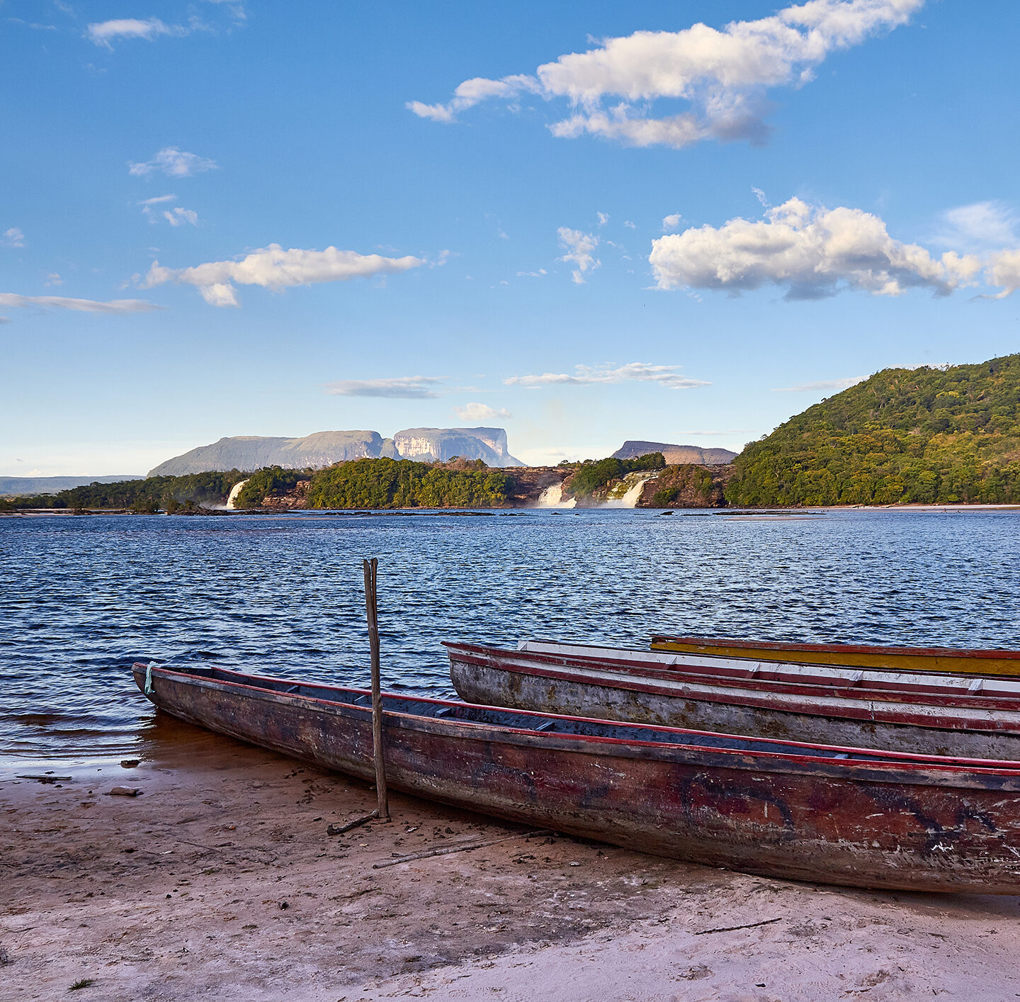 Holzboot am Ufer eines breiten Flusses, umgeben von weiter Landschaft mit bewachsenen Uferzonen.