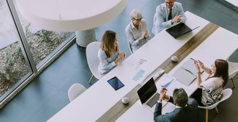Menschen sitzen an einem Konferenztisch und diskutieren, mit Laptops und Unterlagen vor sich.