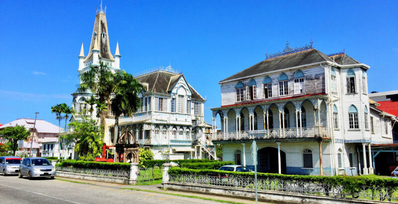 Reihe kolonialer Häuser mit Veranden und weißen Fassaden an einer Straße in Guyana.