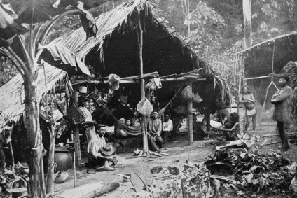 Schwarz-weiß-Ansicht eines einfachen Dorf- oder Campgeländes mit Hütten und Holzstrukturen.