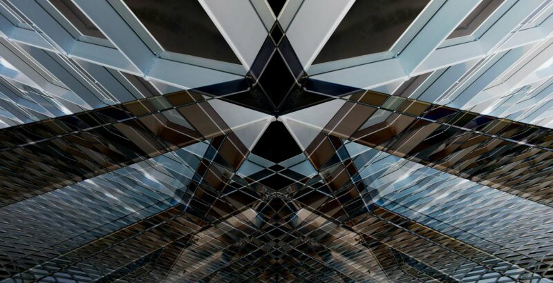 Abstrakte Aufnahme einer modernen Glas- und Metallkonstruktion aus diagonalen Linien und reflektierenden Oberflächen – Sinnbild für Struktur, Stabilität und komplexe Systeme.