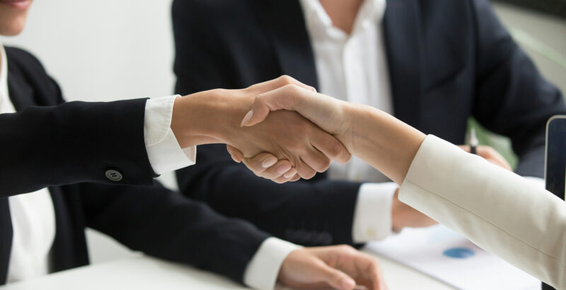 Zwei Personen in Businesskleidung geben sich zur Begrüßung oder zum Abschluss eines Meetings die Hand.