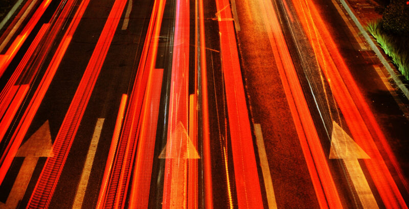 Langzeitbelichtetes Foto einer Autobahn bei Nacht mit roten und weißen Lichtspuren vorbeifahrender Autos.